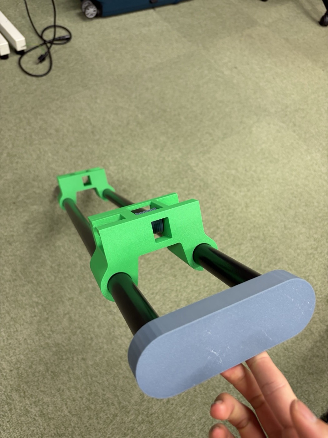 床に置かれた2本の黒いポールが緑色の3Dプリント部品2つで連結されている。先端には手で持っているグレーの楕円形キャップが取り付けられている